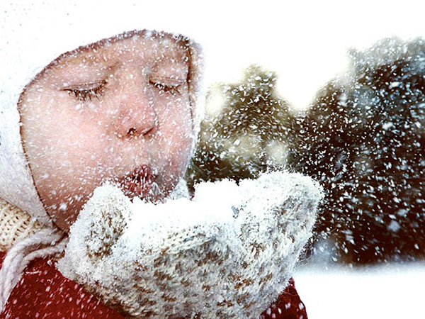 Девочка дует на снег в варежках