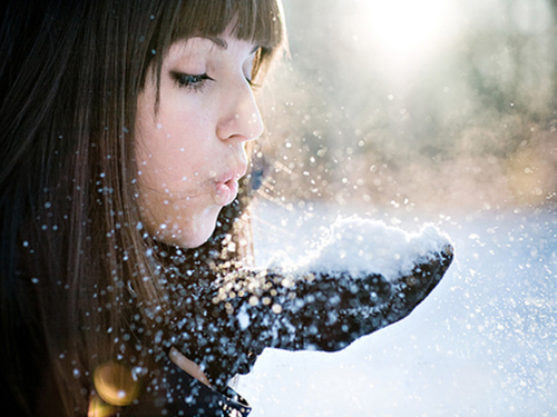 Девушка дует на снег на ладони
